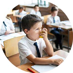 A young boy uses an inhaler while sitting in a school lesson