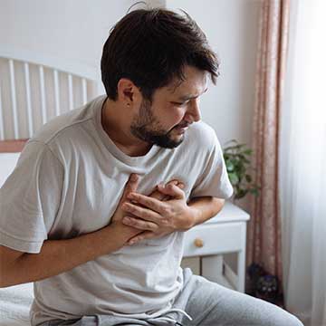 A man sitting on a bed clutches his chest