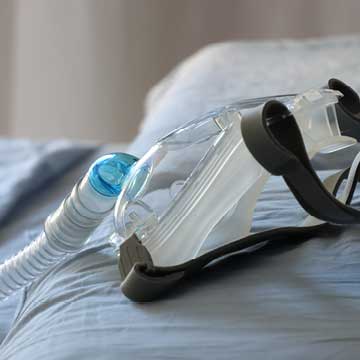 A close-up view of a CPAP mask and its corrugated tube lying on a bed sheet