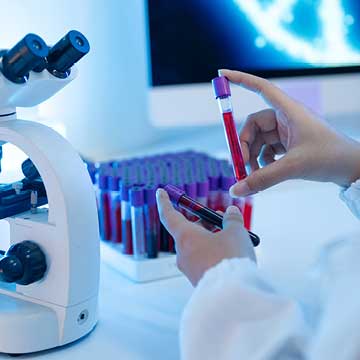 A person in a white lab coat holds vials of blood