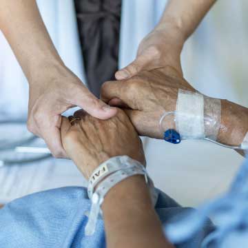 Palliative care, someone in scrubs holding the hands of someone with an IV in a medical gown