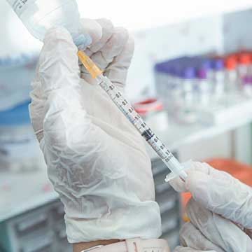 A person in white gloves draws a corticosteroid from a vial into a syringe